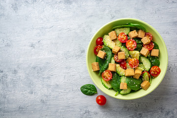 Vegan salad with spinach, cucumber, tomatoes, avocado, fried tofu and sesame. Top view. Copy space. - obrazy, fototapety, plakaty