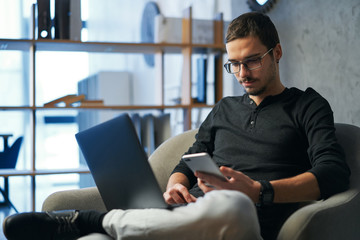 Young man working with computer, phone and tablet at the table while drinking coffee