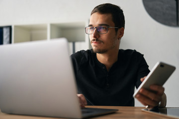 Young man working with phone and computer, receiving phone call, talking with partners 