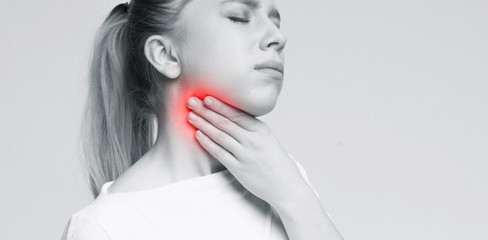Woman suffering with sore throat, touching her neck