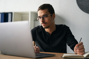 Young man working with computer, phone and tablet at the table while drinking coffee