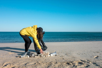 Woman picking up trash and plastics cleaning the beach with a garbage bag. Environmental volunteer...
