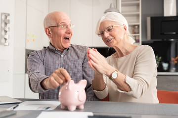 Senior couple putting coin into piggy bank