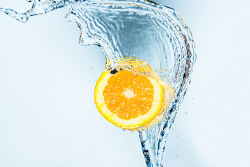 Wave of water splashing in a half orange against a light blue background