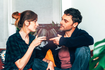 attractive couple sitting on a sofa and looking each others, toasting and celebrating together with a glass of good wine