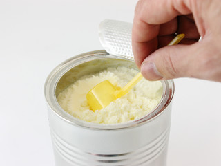hands holding spoon of baby milk formula