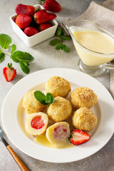 Cottage cheese dumplings with fresh strawberry, served with sour-honey sauce, delicious summer dessert on a bright stone table.