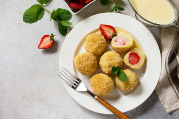 Cottage cheese dumplings with fresh strawberry, served with sour-honey sauce, delicious summer dessert on a bright stone table. Top view flat lay background, copy space.