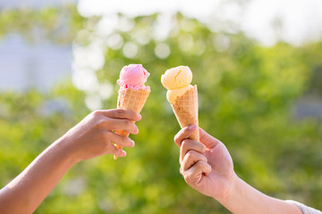 People holding and eating ice cream in the park. Hands holding melting ice cream waffle cone in...