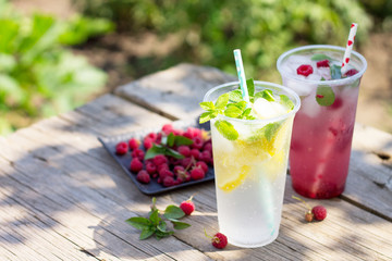Cold beverage. Refreshing summer drink lemon, refreshing summer drink raspberry with basil and ice on a wooden kitchen table.