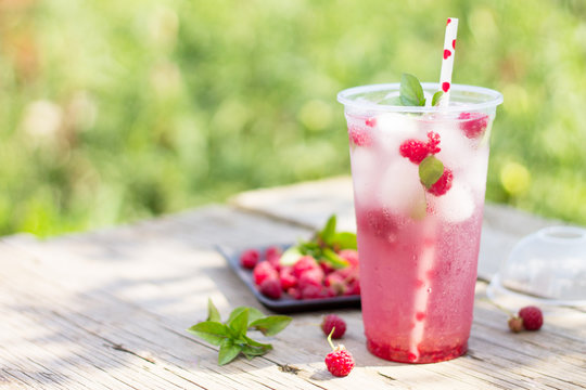 Cold beverage. Refreshing summer drink raspberry with basil and ice on a wooden kitchen table. Copy space.