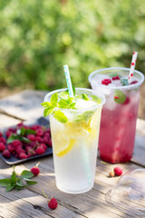 Cold beverage. Refreshing summer drink lemon, refreshing summer drink raspberry with basil and ice on a wooden kitchen table. Copy space.