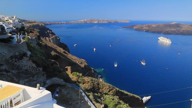 Photo from iconic village of Oia in volcanic island of Santorini, Cyclades, Greece. Sail boats and yachts docked in peaceful blue Aegean Sea. Marine landscape at summer sunny morning