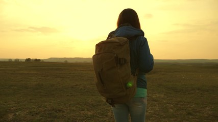 girl traveling with a backpack against the sky and the flare of sun. tourist young woman goes on a sunset to the mountains. desire for knowledge of the world. sports tourism concept.