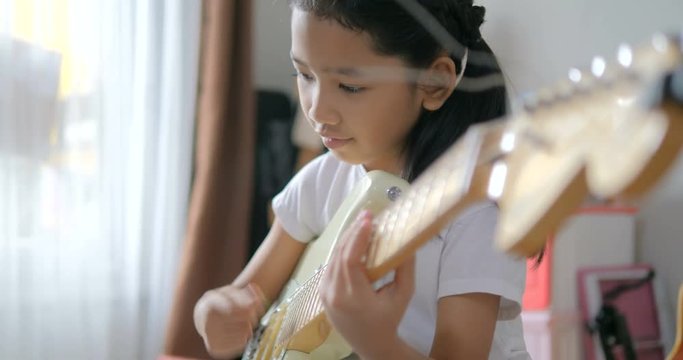 Asian little girl learning to play basic guitar by using electric guitar for beginner music instrumental self studying at home