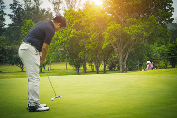 Golfer putting golf into the hole  in beautiful golf course. The evening golf course with sunset in thailand