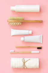 Set of eco cosmetics products and tools for shower or bath Bamboo toothbrush, natural brush, white bottles, towel accessories for body, face and teeth care on pink background. Top view Flat lay