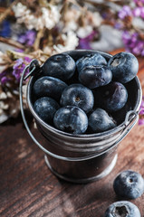 a small bucket of blueberries and flowers. on a wooden board.