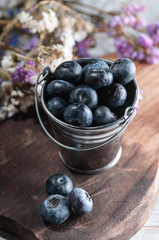 a small bucket of blueberries and flowers. on a wooden board.