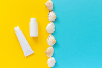 White tube, bottle of sunscreen and line seashells on yellow and blue paper background. Mock up Template for lettering, text or your design Creative Top View Copy space.