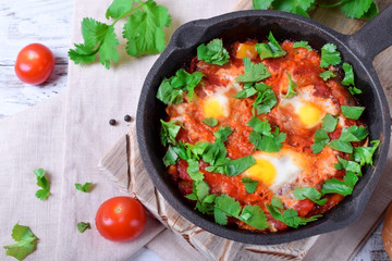 Shakshuka with tomato sauce and quail eggs topped with cilantro in a cast iron pan. Jewish cuisine meal