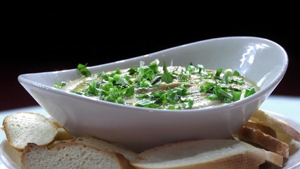 Hummus fresh with greens in a ceramic plate close-up.