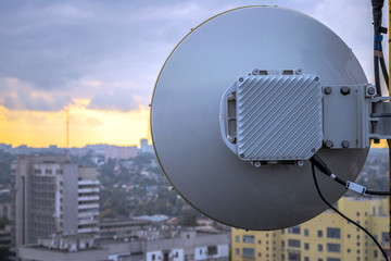 Telecommunication equipment for wireless data transmission is a close-up.Powerful round antenna is on the roof of the building. The base station of mobile communication works at height.