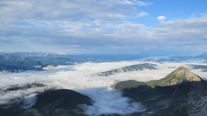 view from mountain top with mountain ranges, cloud cover and green valleys below and blue sky in the background