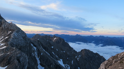 early morning in the mountains with snow-covered rock formation in the foreground and cloud cover and sky in the background, traces from pink and orange in the sky from sunrise