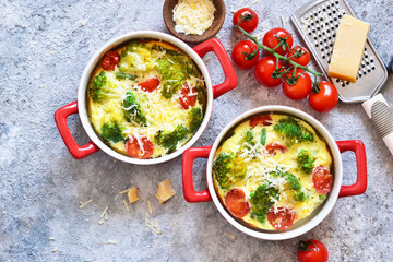 Casserole with broccoli, tomatoes and parmesan on a concrete background. View from above.