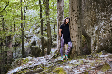 Fototapeta premium Young attractive girl stand in forest and lean on a tree