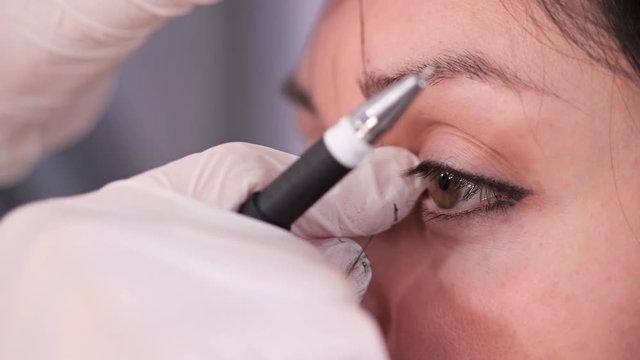 Close-up, girl's eyes. The specialist draws the correct shape of the eyebrows with a thread. Beauty clinic. 4K Slow Mo