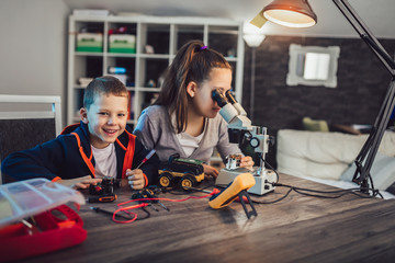 Happy smiling boy and girl constructs technical toy and make robot. Technical toy on table full of details