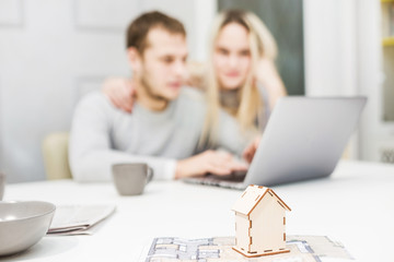 Lovely young couple, using a laptop and choosing a new apartment. Layout of the house in the foreground.