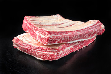 Raw wagyu short loin ribs as closeup on black background with copy space
