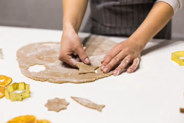 Young pretty woman prepares the dough and bakes gingerbread and cookies in the kitchen. She makes a star shape on the dough. Merry Christmas and Happy New Year.