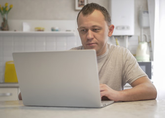 Man sits in his kitchen with a laptop.