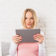 Happy smiling pregnant woman lies in bed and looks at tablet.