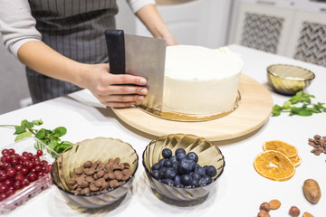 Confectioner smooths white cream on a biscuit cake with a cooking spatula. The concept of homemade pastry, cooking cakes.