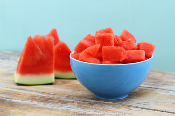 Juicy and refreshing cubes of watermelon in blue bowl on wooden surface