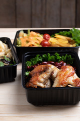 crispy roast chicken and vegetables in black plastic containers, rustic wooden table