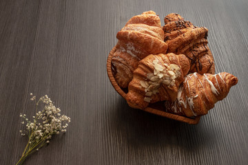freshly baked croissants with almonds, chocolate and powdered sugar  on a wooden dark table closeup, top view