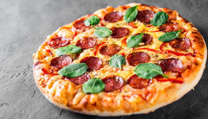 Pepperoni Pizza with Mozzarella cheese, salami, pepper, Spices and Fresh spinach. Italian pizza on Dark grey black slate background