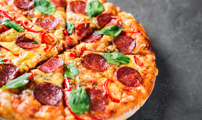 Pepperoni Pizza with Mozzarella cheese, salami, pepper, Spices and Fresh spinach. Italian pizza on Dark grey black slate background