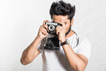 Portrait of a handsome young stylish man with beard taking photo on a vintage camera.