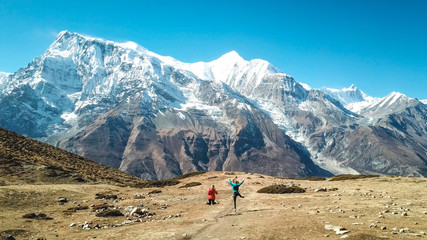 A couple jumping on the Annapurna Circuit Trek, Himalayas, Nepal. Annapurna chain in the back, covered with snow. Clear weather, dry grass, snowy peaks. High altitude, massive mountains. Freedom