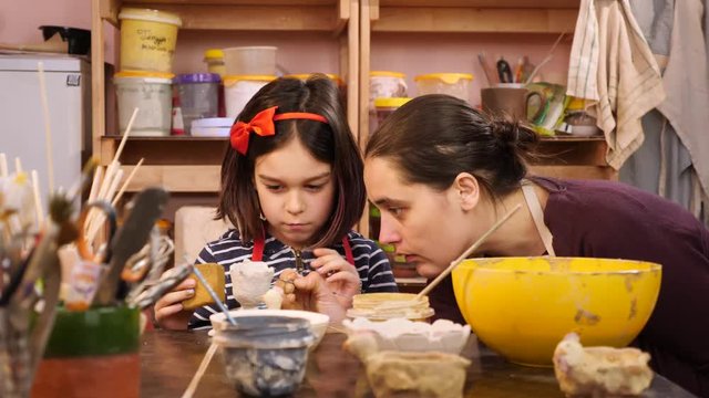 Young girl and teacher at art workshop. Painting clay figures.