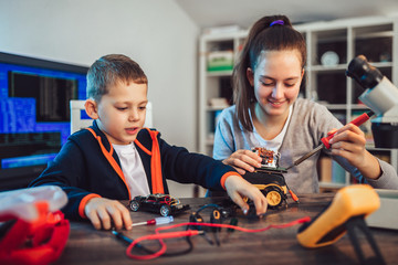Happy smiling boy and girl constructs technical toy and make robot. Technical toy on table full of details