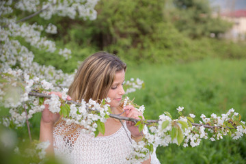 Happy young woman sniffing sthe flowers of a cherry tree in a meadow of a park