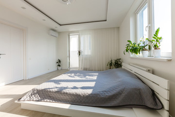 Grey blanket on bed with wooden bedhead in simple bedroom interior with dark poster and chair under window